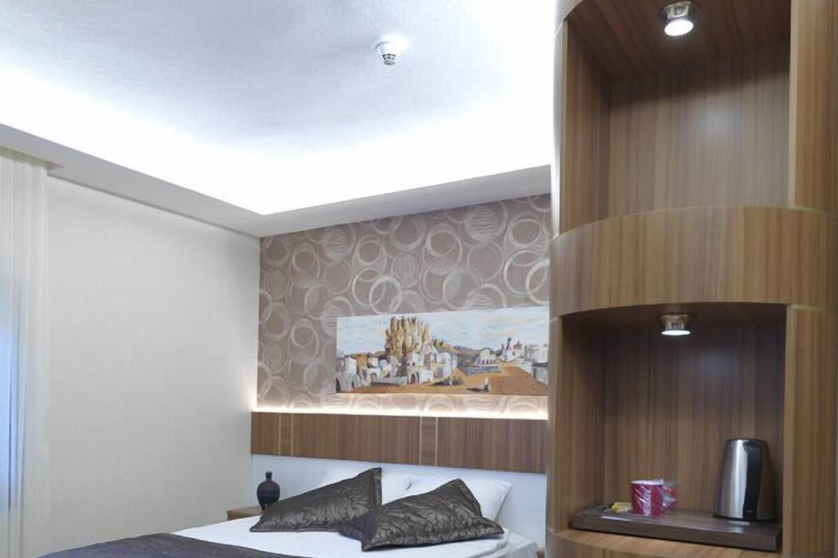 A bedroom with a bed, a wall-mounted shelf with a kettle, and a mini-fridge.