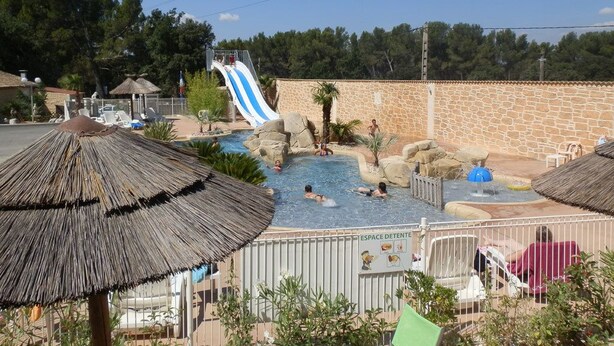 Un área de piscina con tobogán acuático, sillas de descanso y sombrillas.