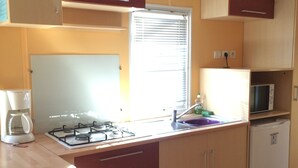 Cocina compacta con estufa a gas, microondas, pileta y alacenas de madera.