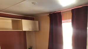 Habitación pequeña con una cama individual y una litera superior, una ventana con cortinas y una mesita de noche.