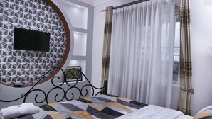 A bedroom with a bed, a wall-mounted TV, and a window with curtains. - Red Sox Hotel (Seeta)