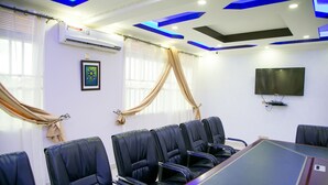 A conference room with a long table, black leather chairs, a flat-screen TV, and blue ceiling accents. - Red Sox Hotel (Seeta)