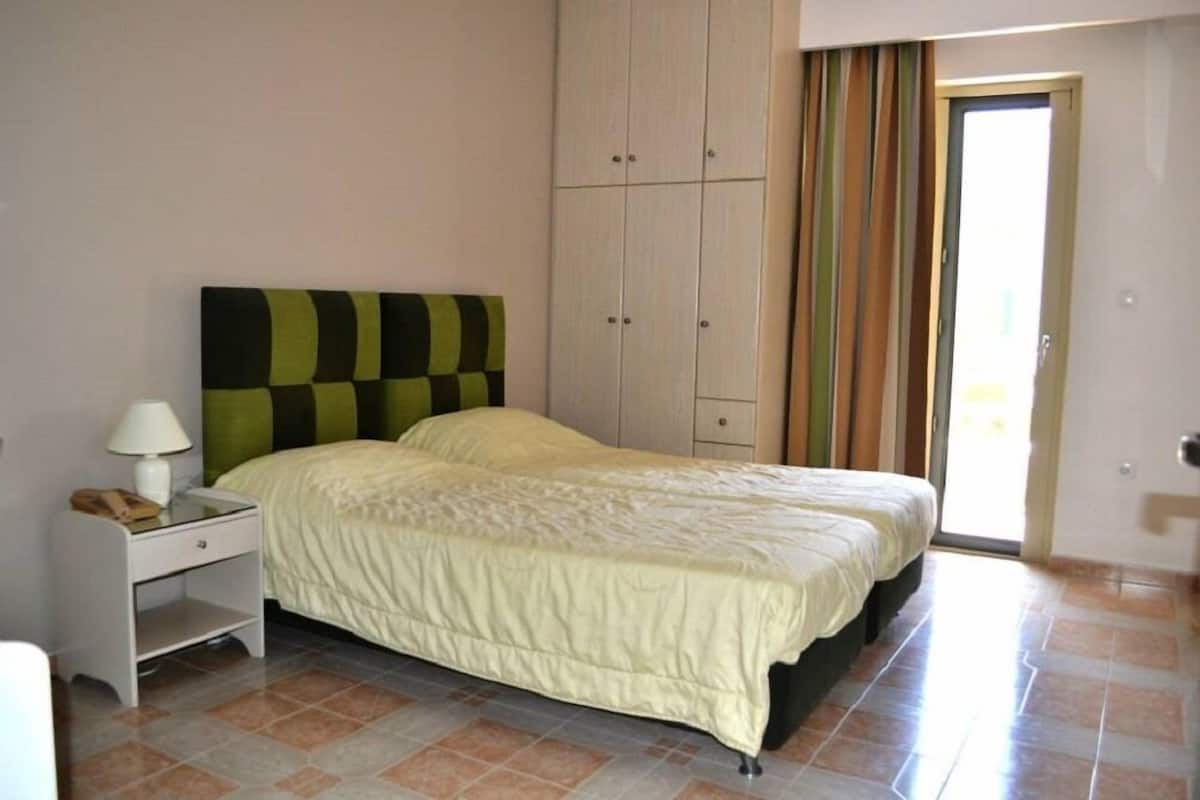 A bedroom with two beds, a nightstand, and a wardrobe.