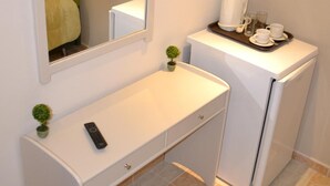 A compact bathroom with a white vanity, a mirror, a small potted plant, a remote control, and a coffee maker on a tray.