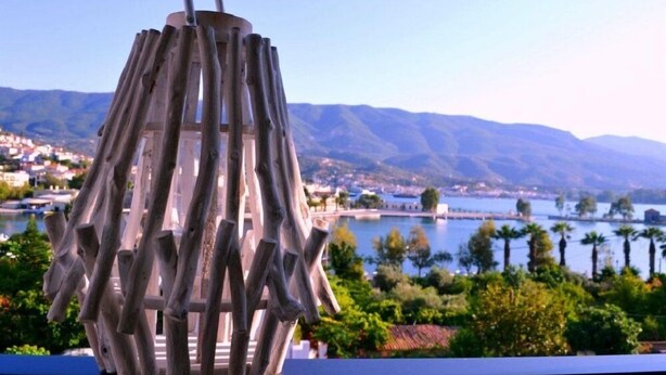 A metal outdoor light fixture with a curved handle, overlooking a lake with mountains in the background.