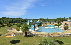 A swimming pool with a water slide, surrounded by palm trees and lounge chairs. - Camping Les Places Dorees (Saint-Jean-de-Monts)