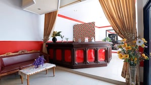 A reception area with a red and white color scheme, a wooden reception desk, a bench, and a vase with flowers. - RedDoorz Plus @ Samratulangi Manado (Manado)