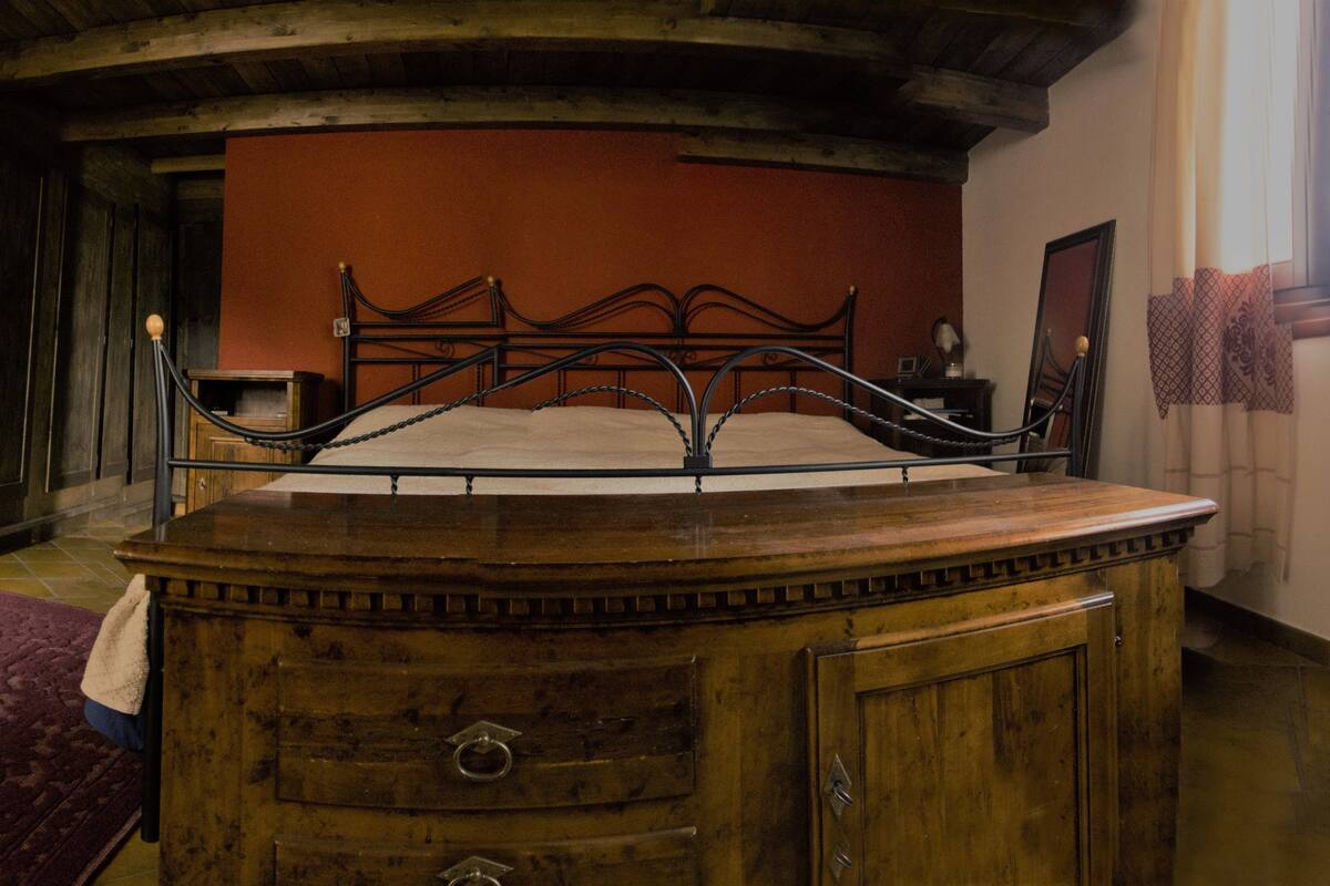 A room with a wooden bed frame, a wooden dresser, a red carpet, and a staircase.