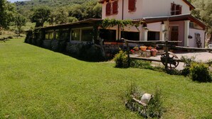 A two-story house with a stone foundation, a red-tiled roof, and a garden with potted plants. - Sas Abbilas (Bonorva)