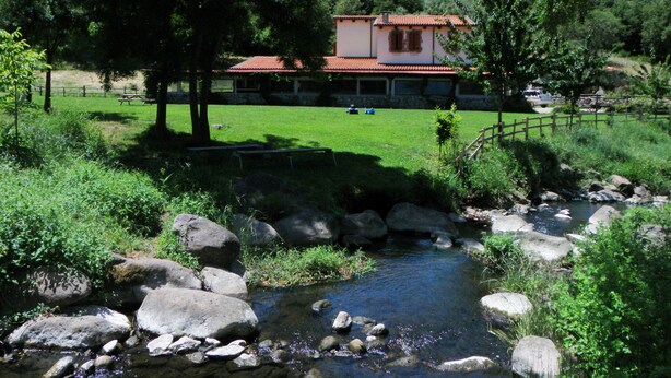 A rustic house with a red-tiled roof, surrounded by a lush green landscape and a small stream. - Sas Abbilas (Bonorva)