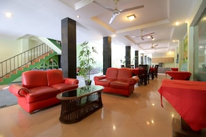 A spacious lobby with red sofas, a glass coffee table, and a staircase leading to an upper level. - RedDoorz Plus @ Taman Siswa 2 (Yogyakarta)