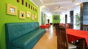 A restaurant with a green wall, wooden-framed picture frames, a blue sofa, red tables, and wooden chairs.