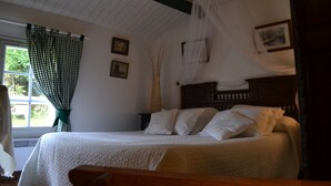 Een slaapkamer met een bed, een raam met gordijnen, een nachtkastje en een aan de muur hangend schilderij.