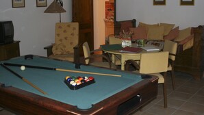 Een pooltafel met ballen, een televisie, een stoel en een tafel met een vaas.