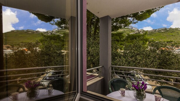 A balcony with a table set for two, overlooking a scenic hillside. - Apartments Andrijanic (Baska Voda)