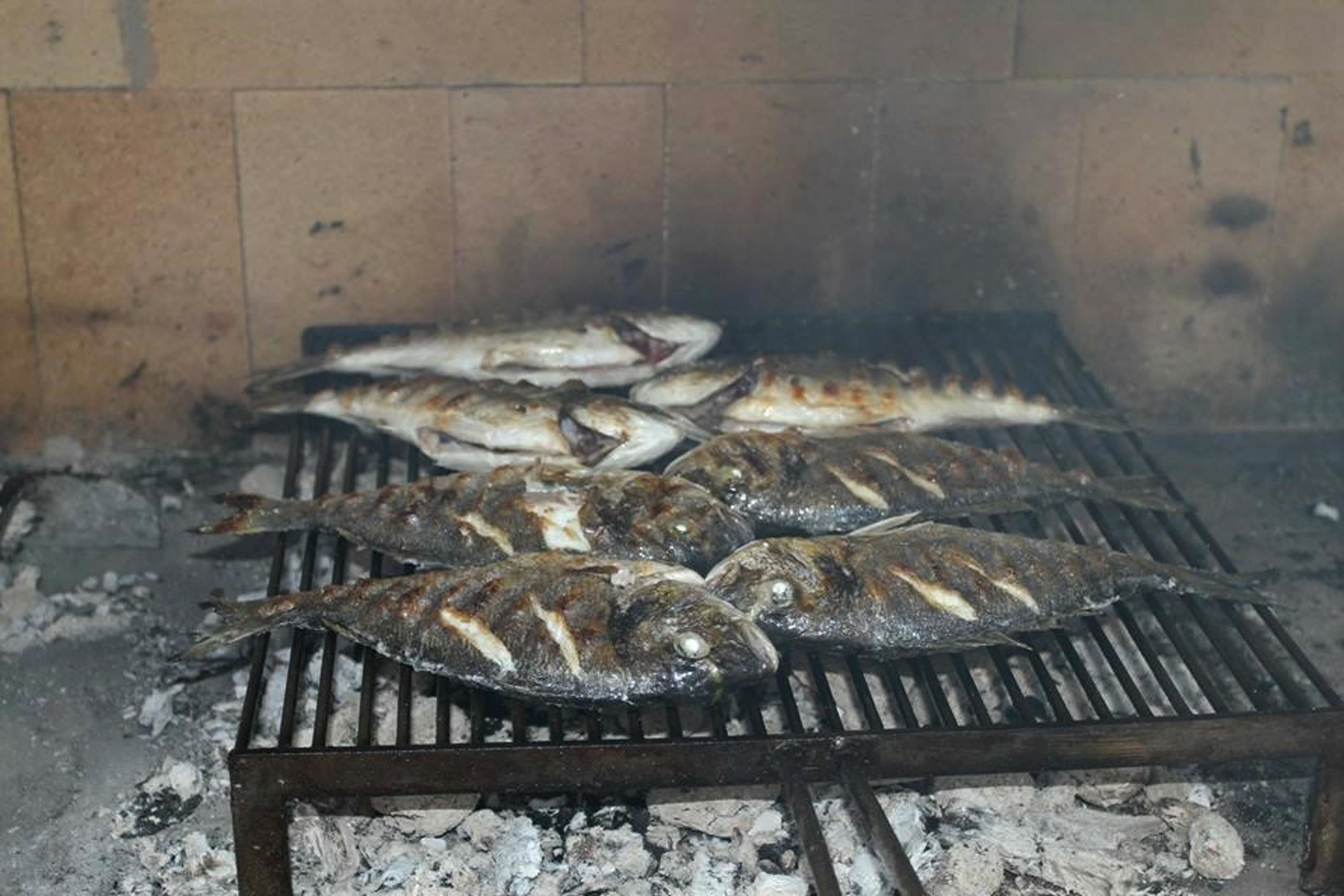 Grillad fisk på en grill, med en tegelvägg i bakgrunden.