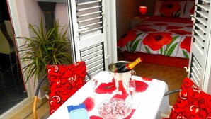 A small room with a bed, a table with a bottle of champagne, and a bowl of food. - Apartments Andrijanic (Baska Voda)