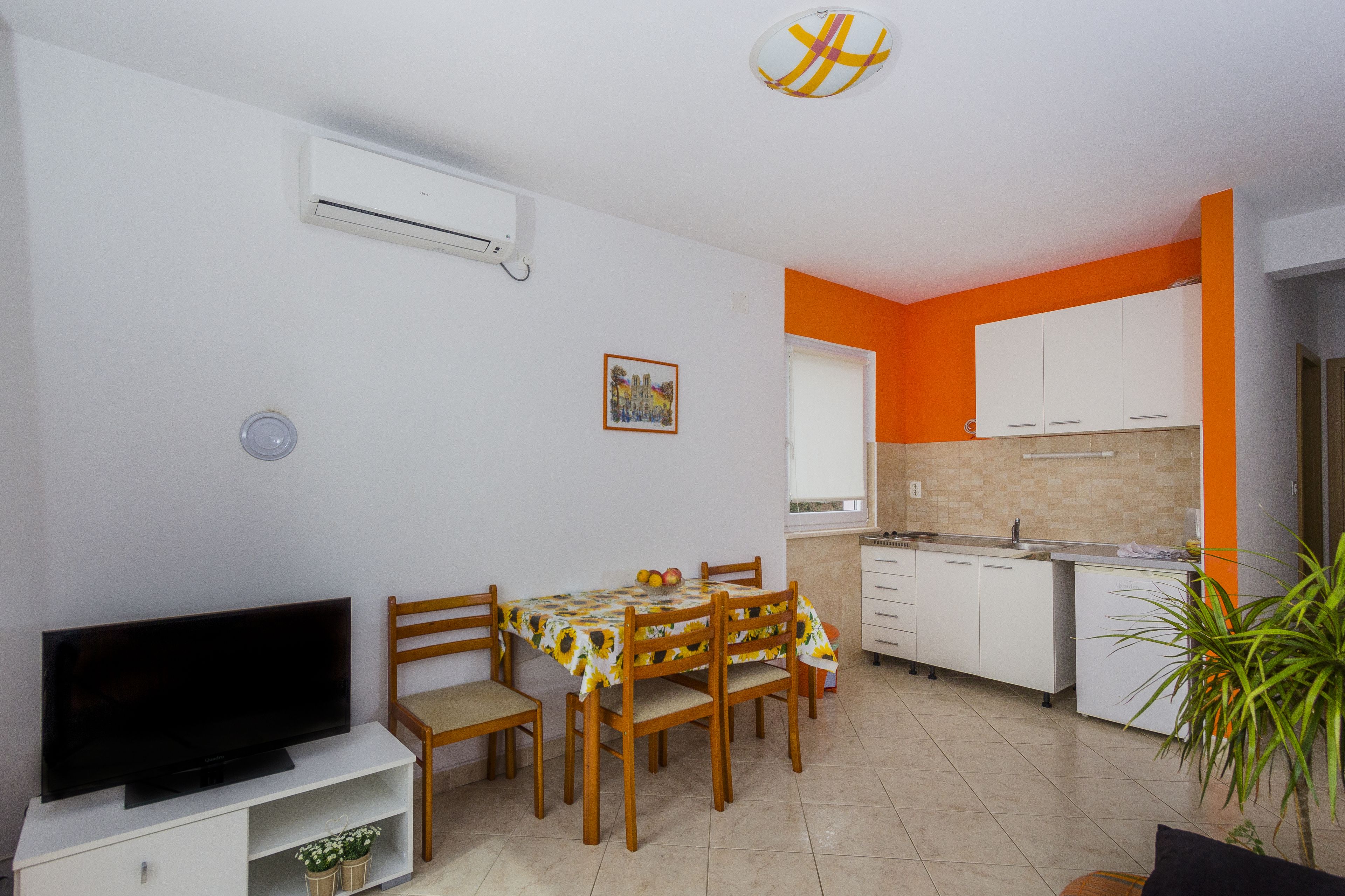 A compact living space with a dining area, a kitchen, and a TV on a white cabinet.