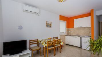 A compact living space with a dining area, a kitchen, and a TV on a white cabinet.