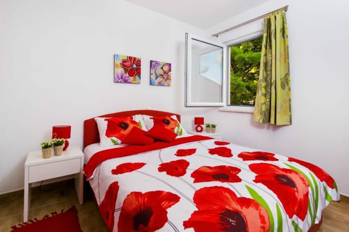 Quarto com cama, mesa de cabeceira, janela e duas obras de arte na parede.