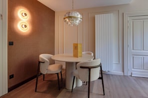 A dining area with a round table, four chairs, a chandelier, and a door with a white panel. - Roosendaelhof (Geel)