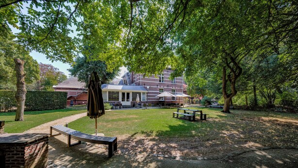 A courtyard with a brick wall, a bench, and a covered seating area with umbrellas. - Roosendaelhof (Geel)