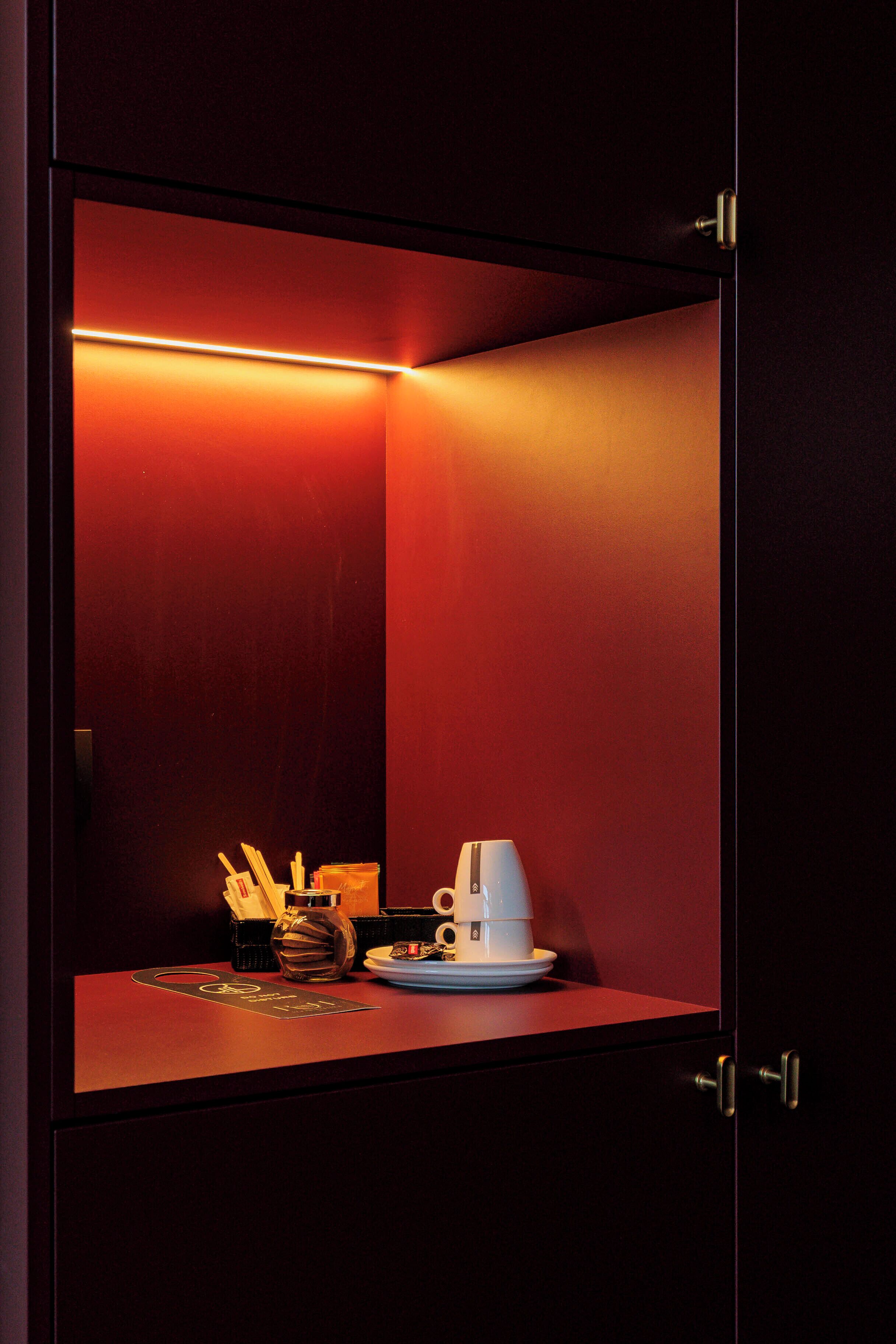 A small, enclosed space with a red interior, a table with a cup and saucer, and a small vase.