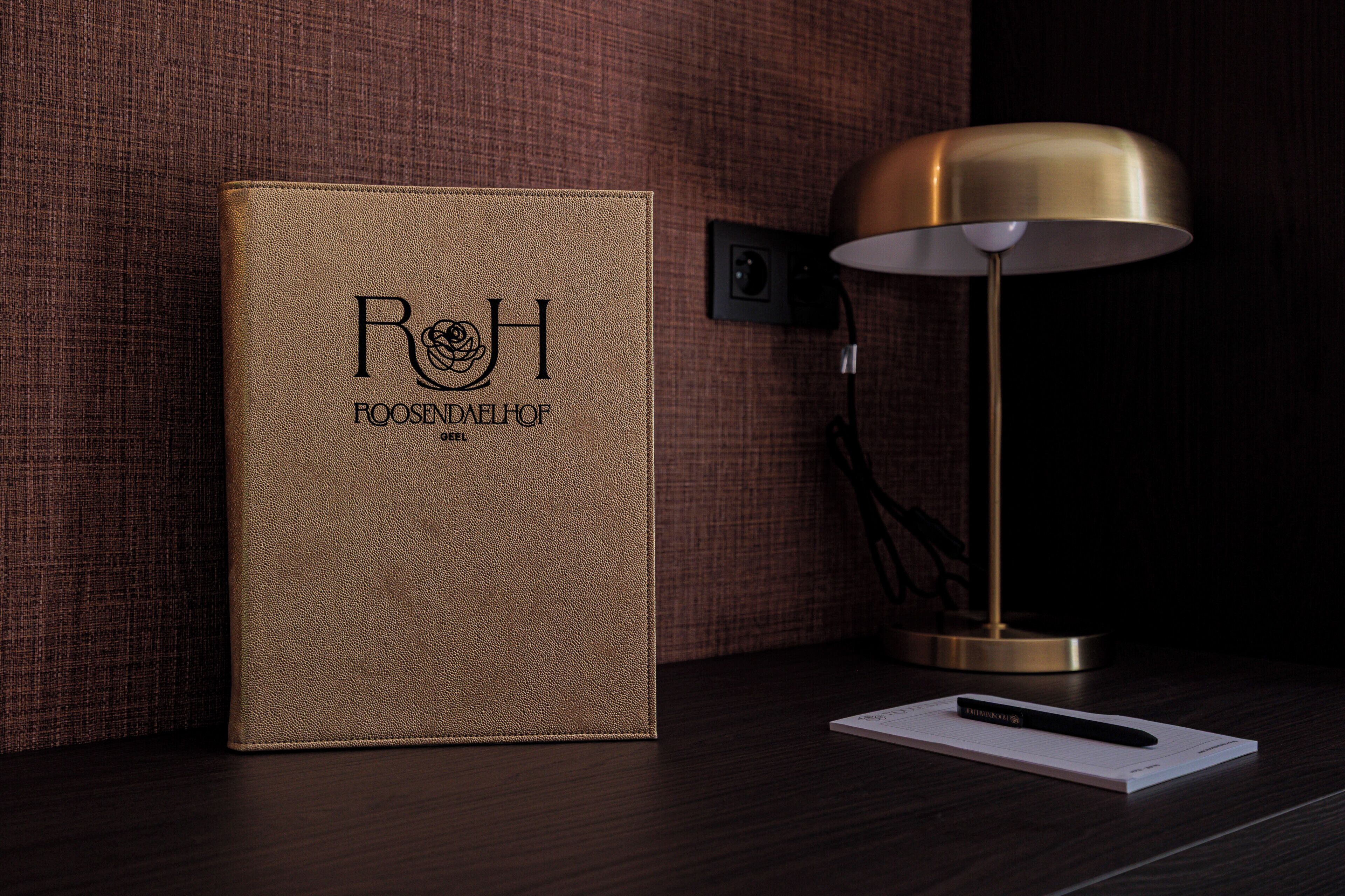A leather-bound book with embossed text, a desk lamp, and a notepad on a wooden surface.