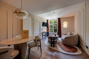 A modern living room with a dining area, a chandelier, a flat-screen TV, and a large window with curtains. - Roosendaelhof (Geel)