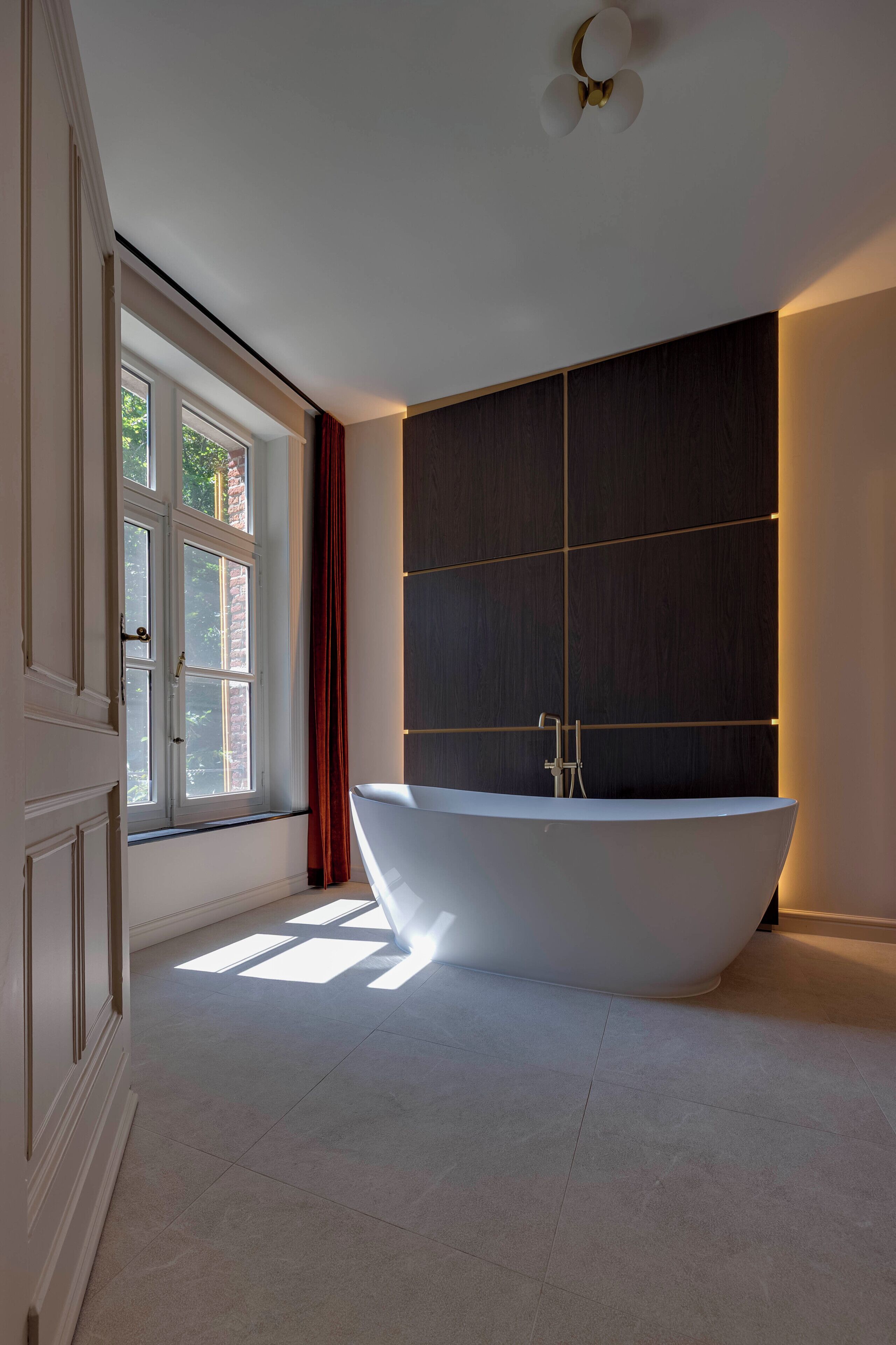 Un baño moderno con una bañera independiente, un ventanal amplio y un panel de pared de madera oscura.