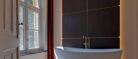 Un baño moderno con una bañera independiente, un ventanal amplio y un panel de pared de madera oscura.