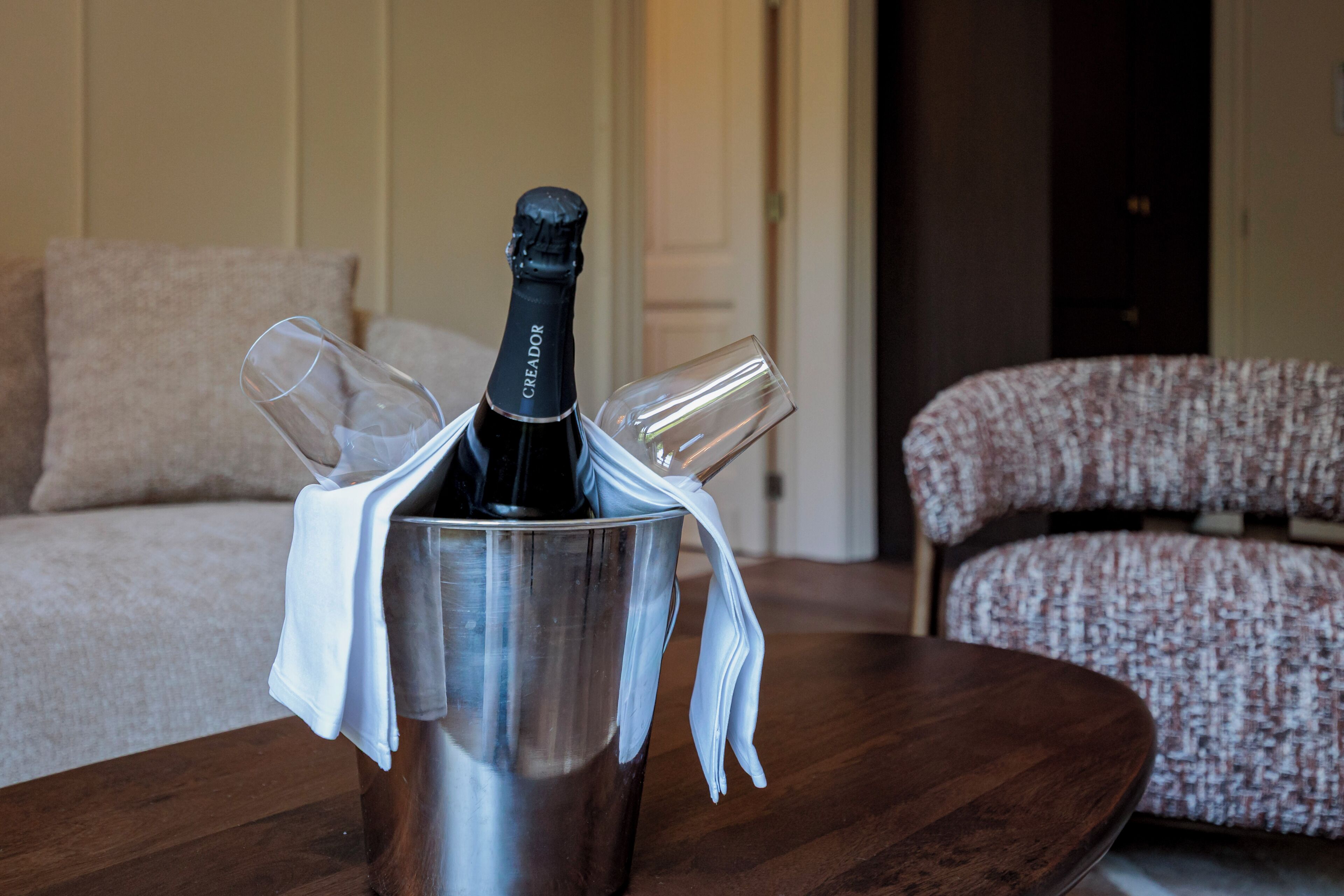 Een fles champagne in een metalen emmer op een houten tafel, met twee glazen ernaast.