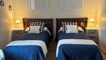 A room with two beds, each with a wooden headboard, white lamps, and blue bedding.