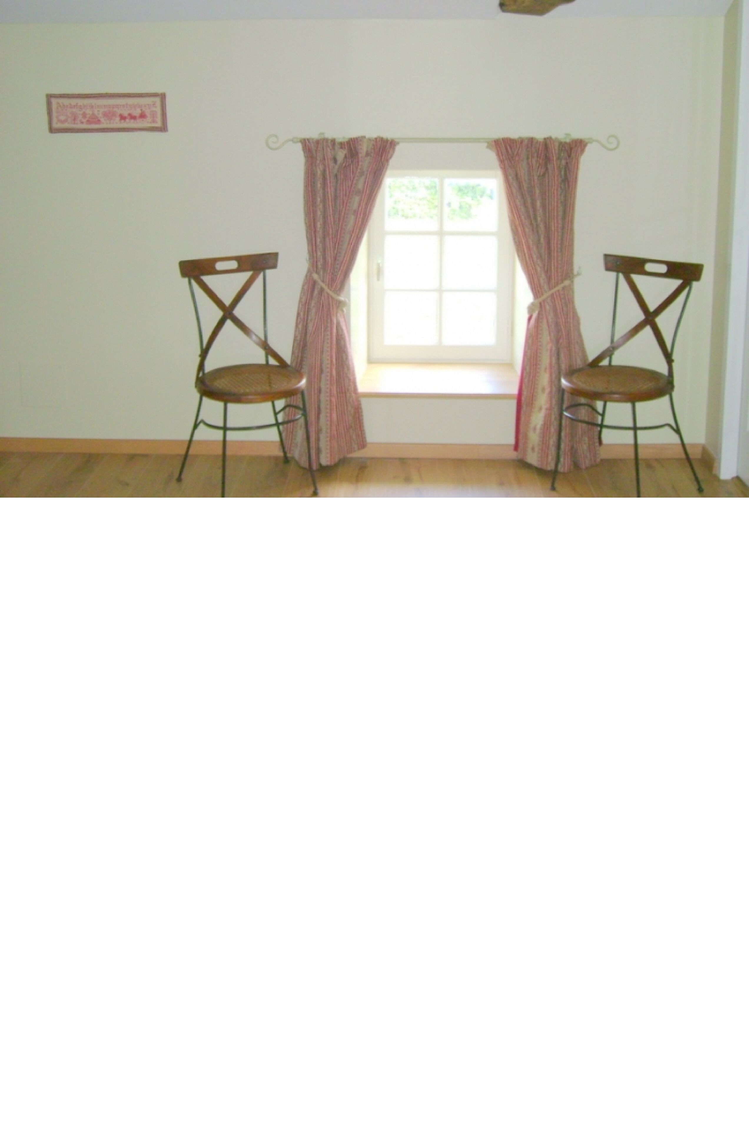 A room with two wooden chairs, a window with curtains, and a framed picture on the wall.