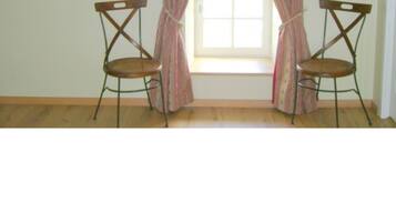 A room with two wooden chairs, a window with curtains, and a framed picture on the wall.