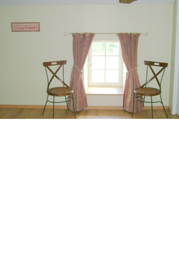 A room with two wooden chairs, a window with curtains, and a framed picture on the wall.