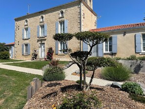 A two-story stone building with blue shutters, a gravel pathway, and a well-maintained garden with various plants and flowers.