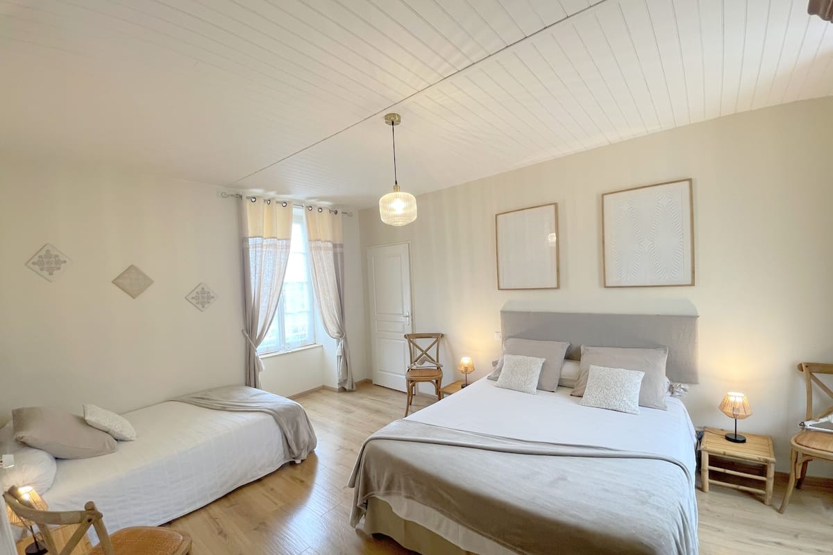 Un dormitorio con dos camas, una ventana con cortinas, una mesita de noche con lámpara y un aplique de pared.