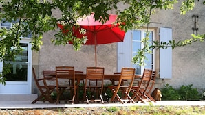 Een houten tuintafel met zes stoelen en een rode parasol.