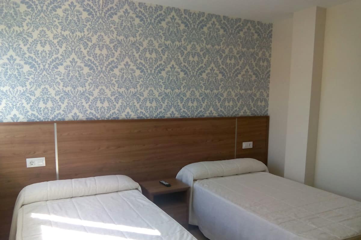 A hotel room with two single beds, a wooden headboard, and a patterned wallpaper.