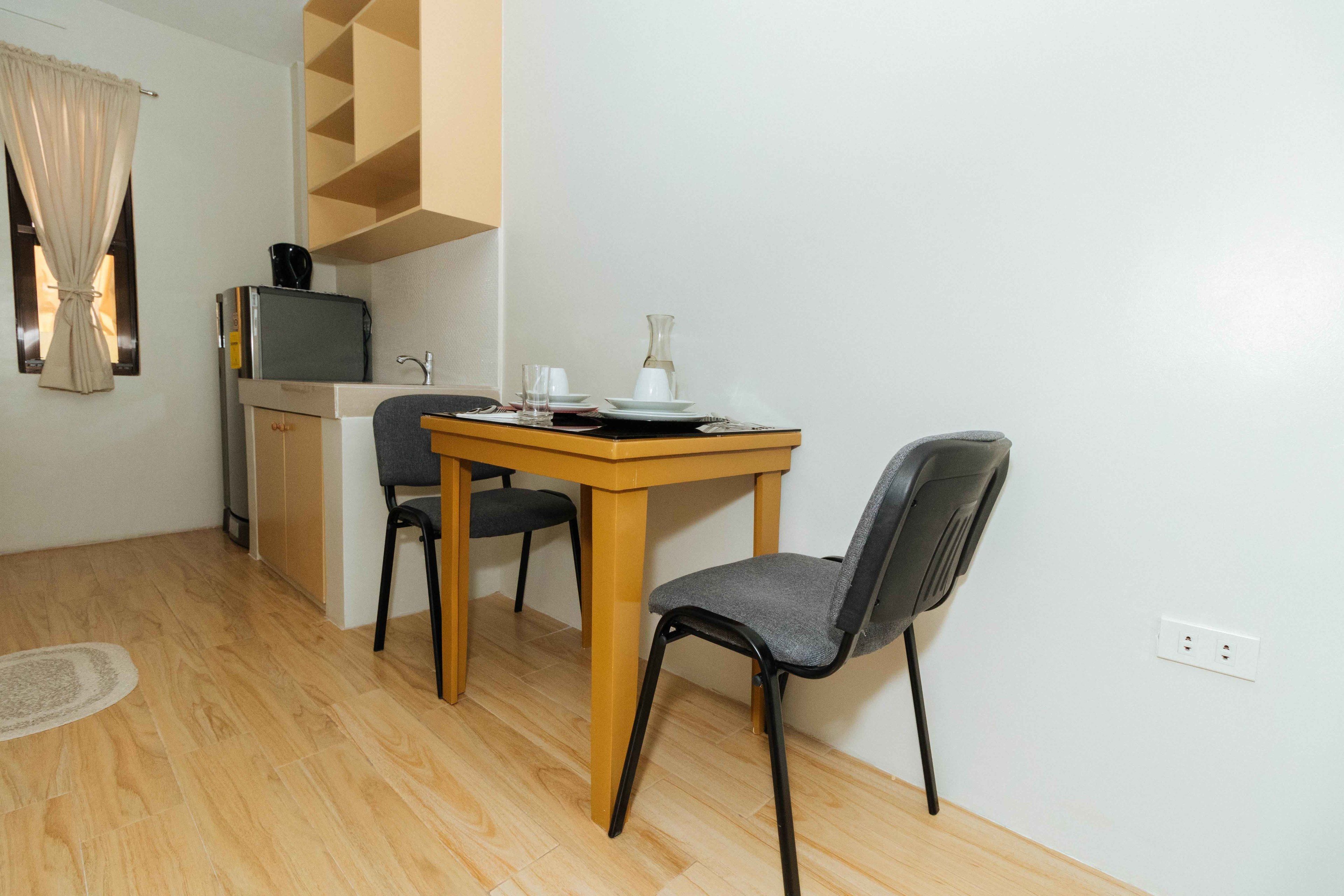 A small kitchenette with a microwave, a coffee maker, and a sink. There is a dining table with two chairs and a vase on it.