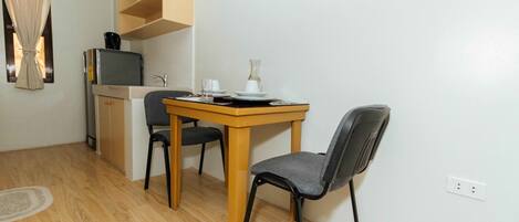 A small kitchenette with a microwave, a coffee maker, and a sink. There is a dining table with two chairs and a vase on it.