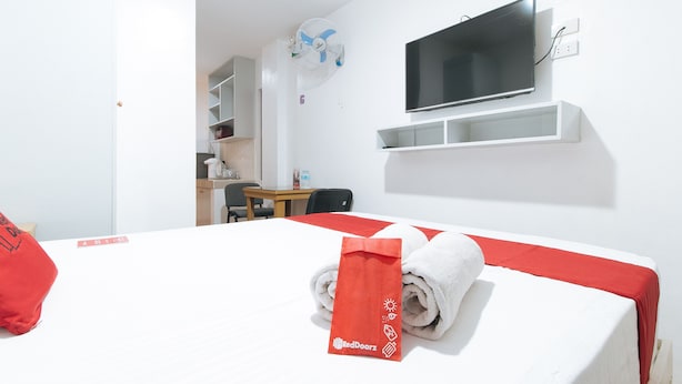 Une chambre d’hôtel comprenant un lit, un téléviseur fixé au mur, un bureau avec une chaise et une petite table avec une bouteille d’eau.