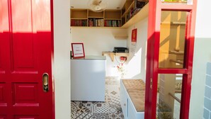 Un couloir avec une porte rouge, un comptoir d’accueil blanc, une bibliothèque et un sol à motifs.