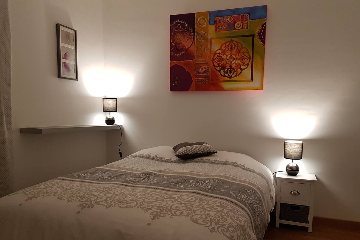 A bedroom with a bed, two bedside lamps, a nightstand, and a wall-mounted artwork.