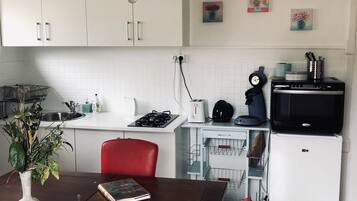 Een keuken met witte kasten, een rode stoel, een eettafel met een boek en een plant, en een zwarte koelkast.