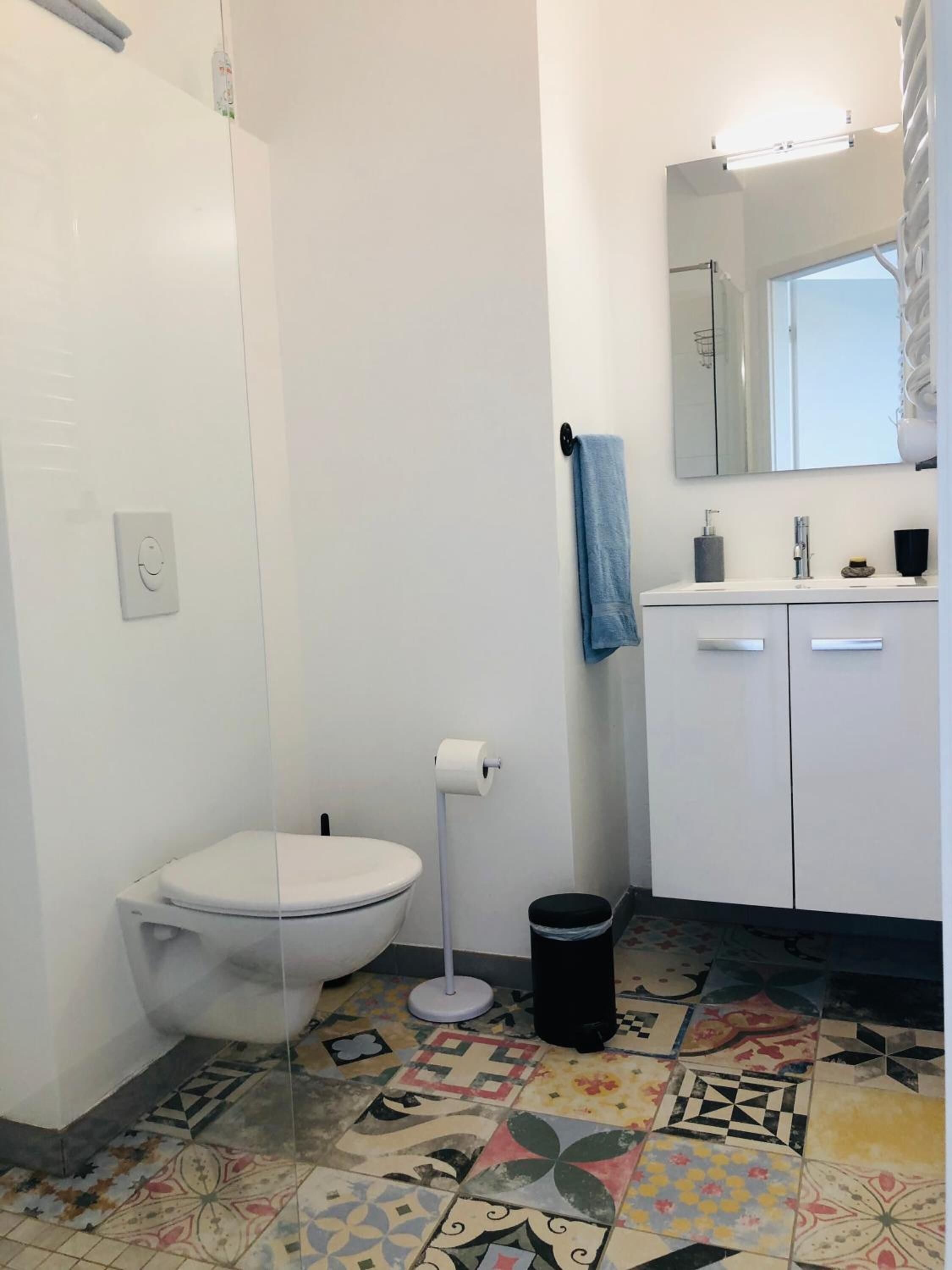 A bathroom with a toilet, a sink, a mirror, and a patterned floor.