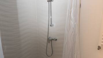 A shower area with a curved showerhead, a handheld showerhead, and a shower curtain with a wavy pattern.