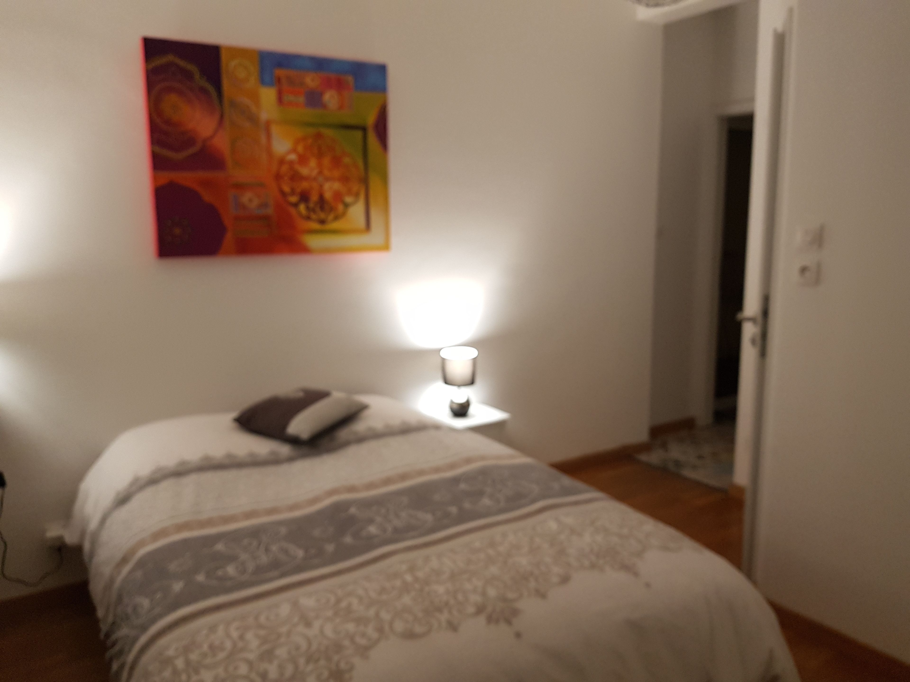 Une chambre à coucher avec un lit, une lampe de chevet et un tableau coloré accroché au mur.