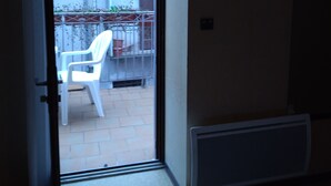 Una habitación con puerta de vidrio corredera que da a un balcón con una silla de plástico blanca.